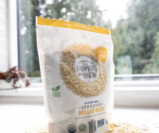 A bag of sprouted rolled oats with some oat on the bottom and a wooden spoon full of oat